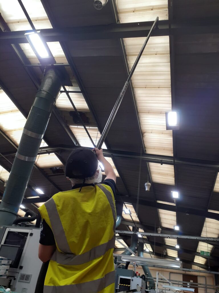 Operator cleaning roof girders in a factory from ground level with a high-reach pole system