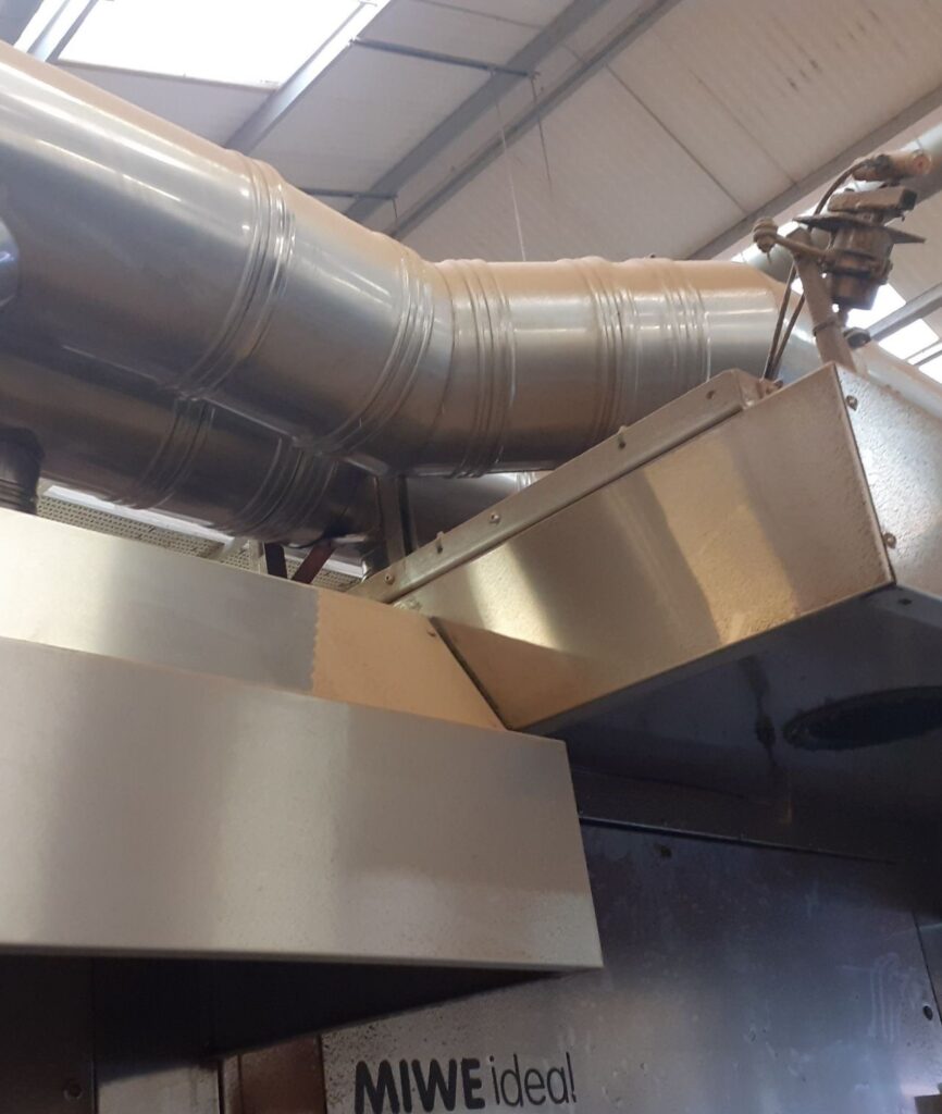 Operator cleaning high-level surfaces above an oven canopy in a commercial kitchen