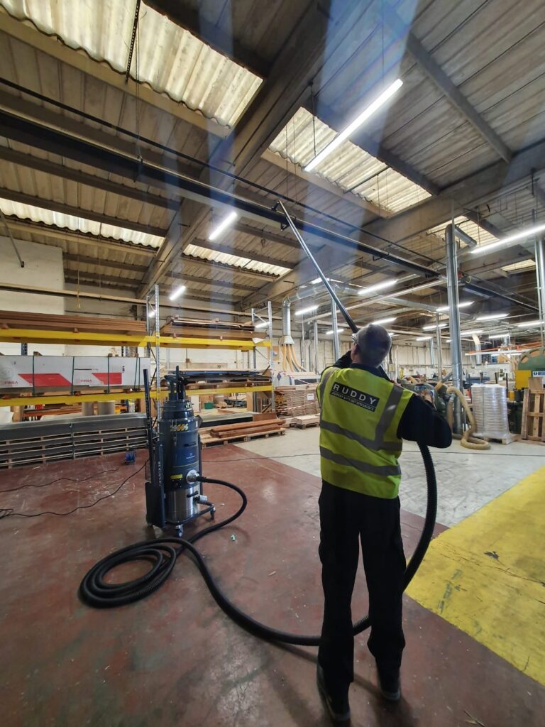 Operator in hi-vis using a mobile industrial vacuum cleaner in a production hall