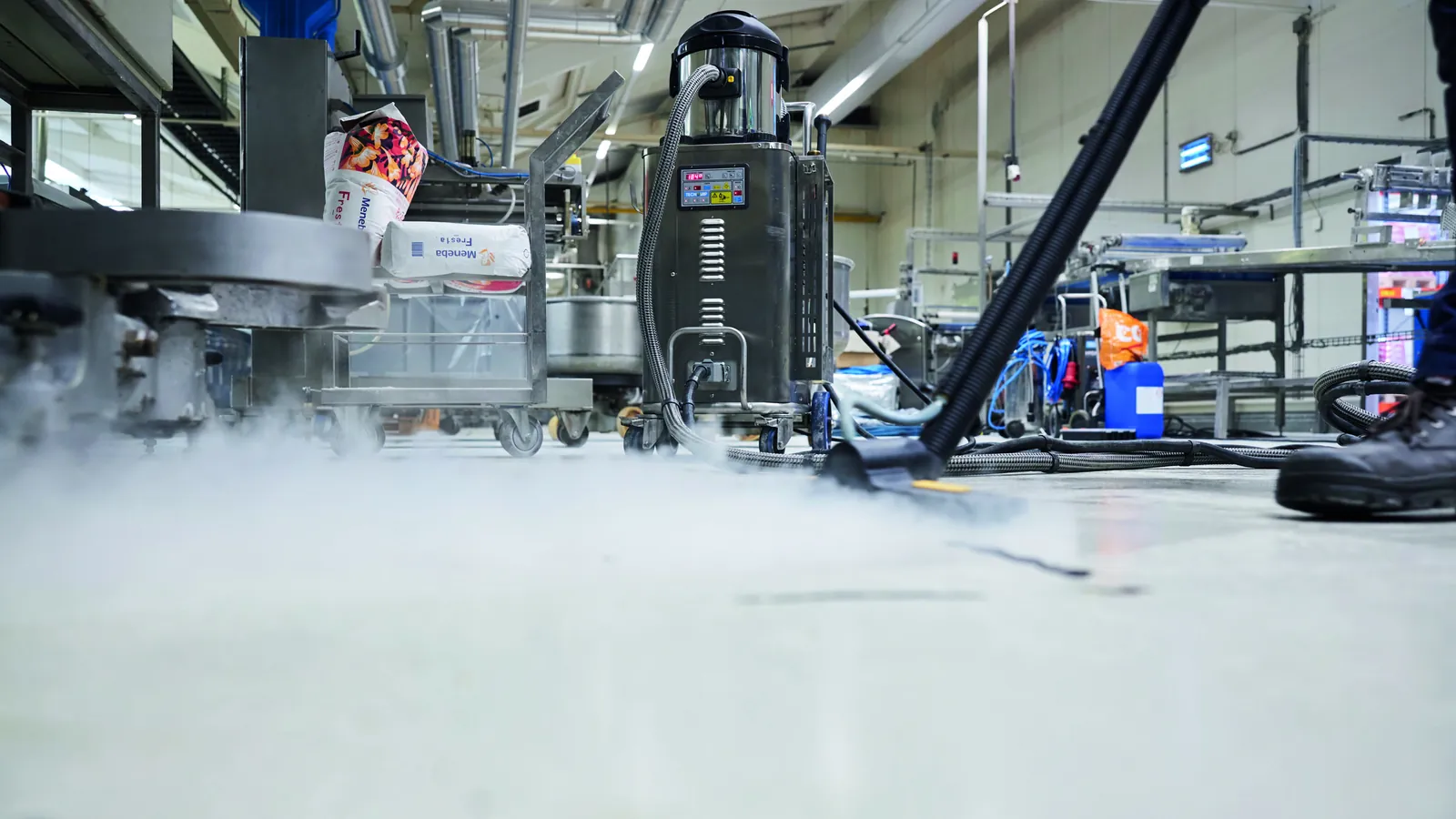 Operator steam-cleaning a factory floor with a mobile unit, the method used in olive oil mill cleaning